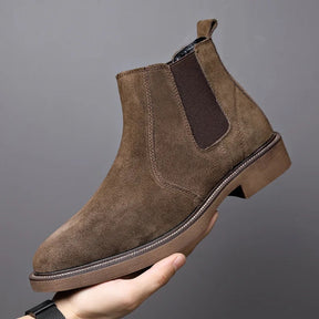 Bota Chelsea masculina marrom em camurça sendo segurada pela mão