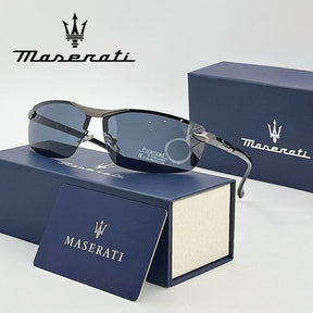 Óculos de sol Maserati com lentes escuras e armação metálica, apoiados sobre estojo azul da marca, com cartão e logotipo Maserati ao fundo.